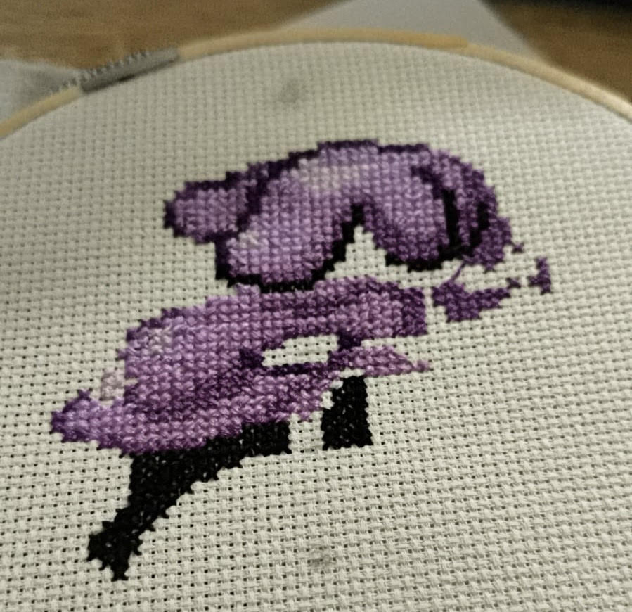 A real in-progress cross-stitch of Muk, stitched in purple and black DMC floss