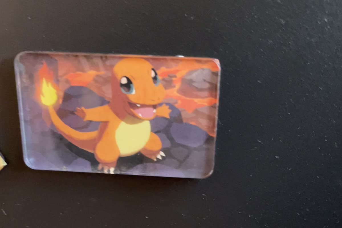 A Charmander card magnet stuck to a black fridge door, the artwork trimmed out of the card and set in a clear acrylic block