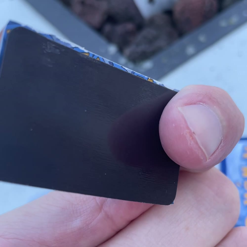A hand holding up a card backed with a black adhesive magnetic sheet, showing the matte magnetic side